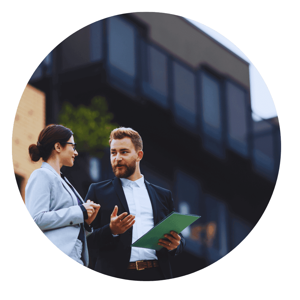 Two real estate professionals, a man and a woman, standing outside a modern building discussing documents, symbolizing client consultation and property planning.