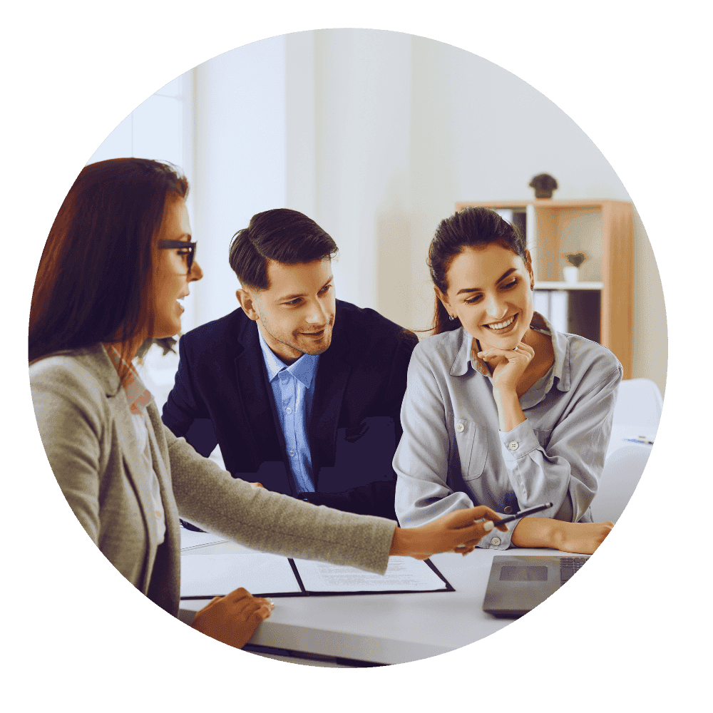 Three real estate professionals, two women and one man, sitting at a desk reviewing documents together, discussing strategy in a bright office.