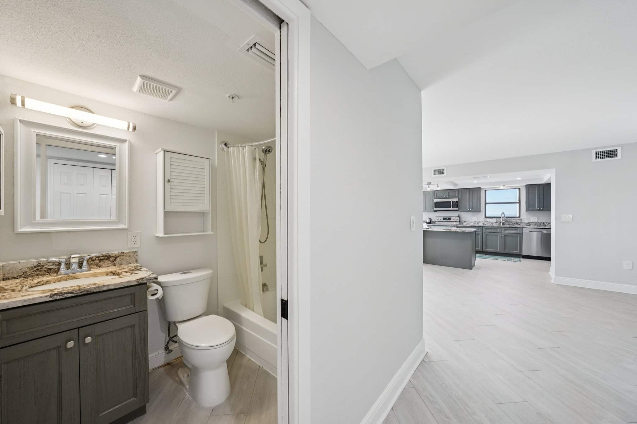 Guest bathroom with tub shower and granite vanity leading to open living area and kitchen at 15316 Gulf Blvd Madeira Beach FL