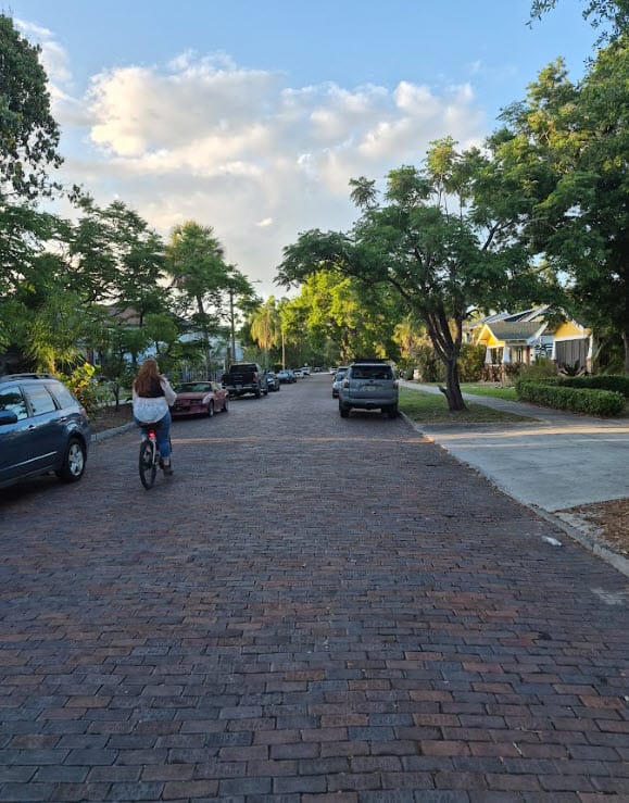 Bicycle rider on a brick-paved street in Euclid St. Paul, St. Petersburg, FL, with trees lining the road and residential homes in the background