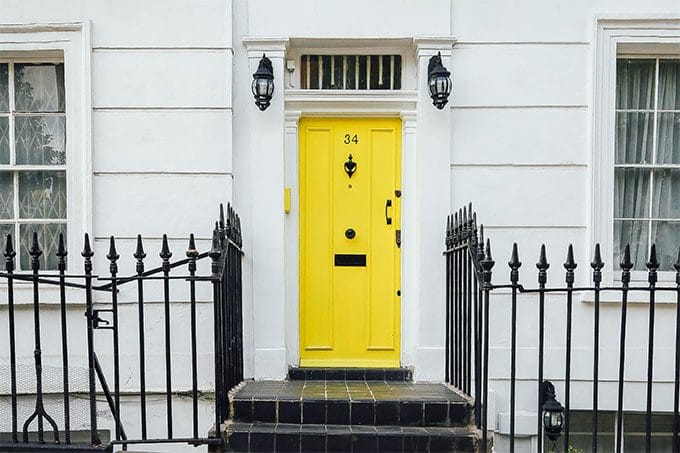 Yellow front door numbered 34 on a white townhouse, flanked by black iron railings and two black lantern-style lights, with windows on either side.
